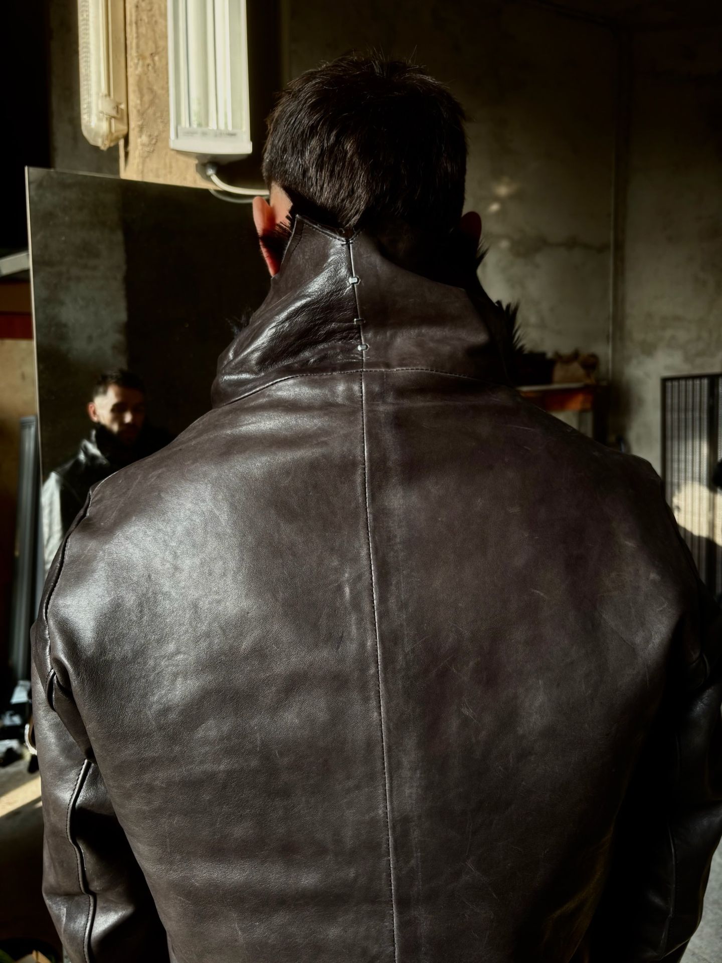 La giacca in pelle marrone indossata, vista da dietro, con il collo alto.