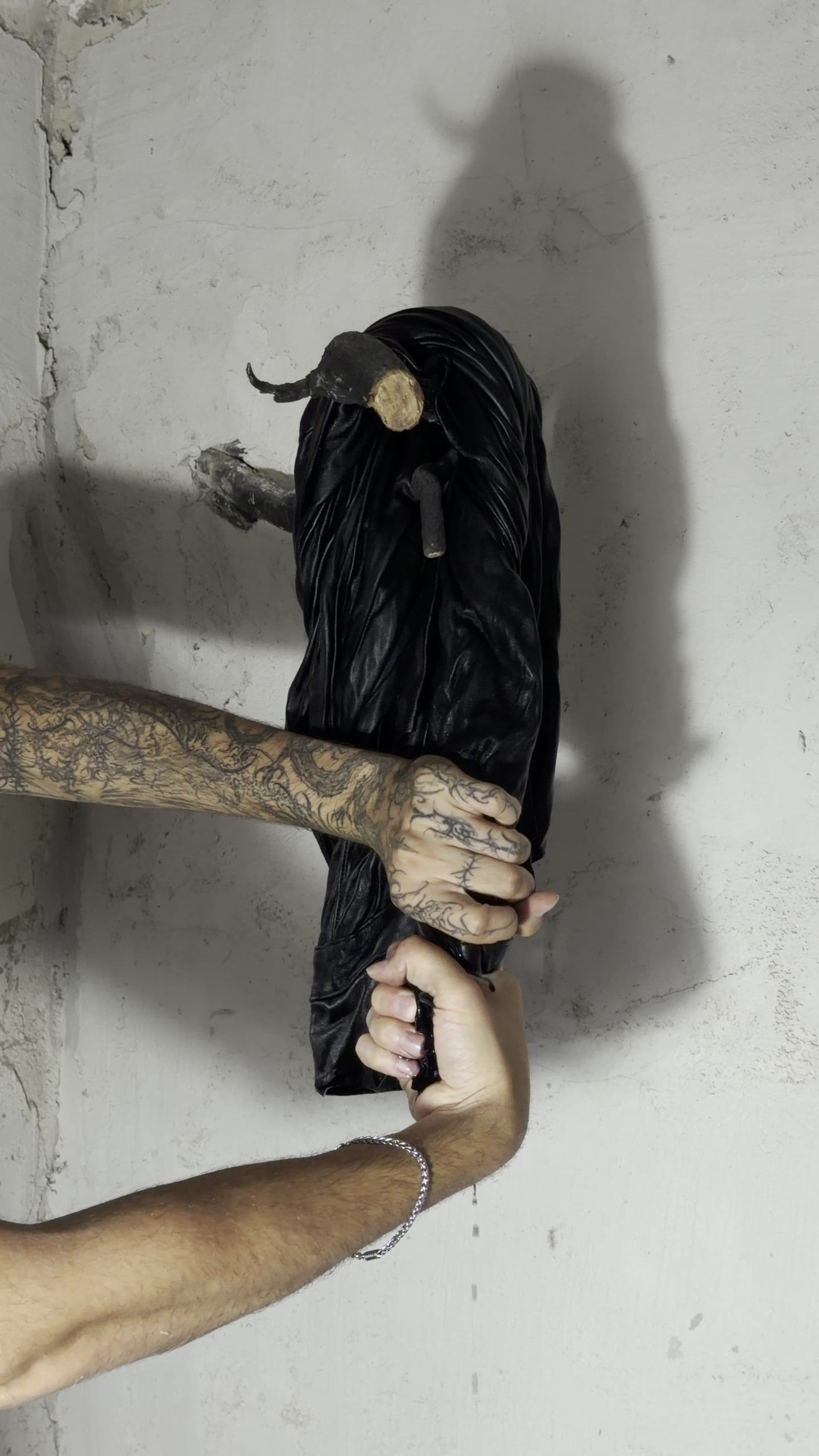 A hand pulls a black leather jacket hung on a hook against the concrete wall.