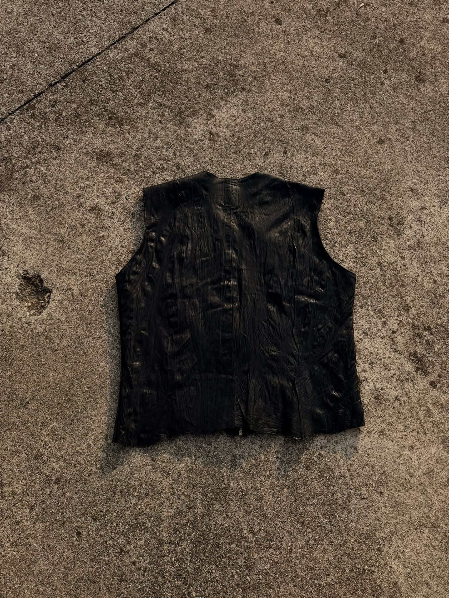 Gilet smanicato in pelle nera disteso sul cemento.