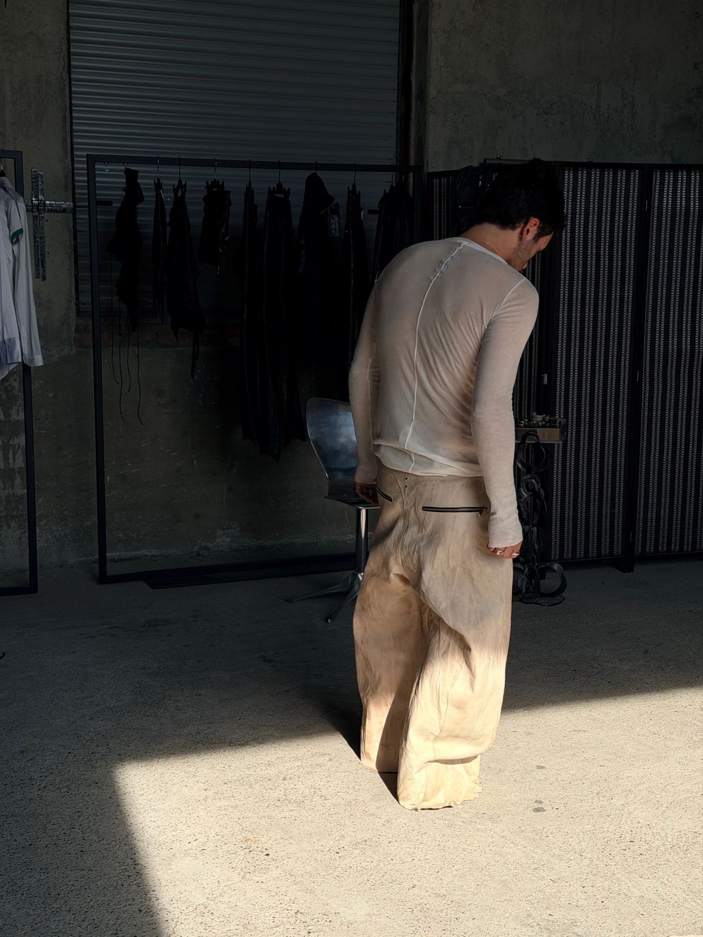 Uomo di spalle con i pantaloni chiari ampi, in laboratorio.