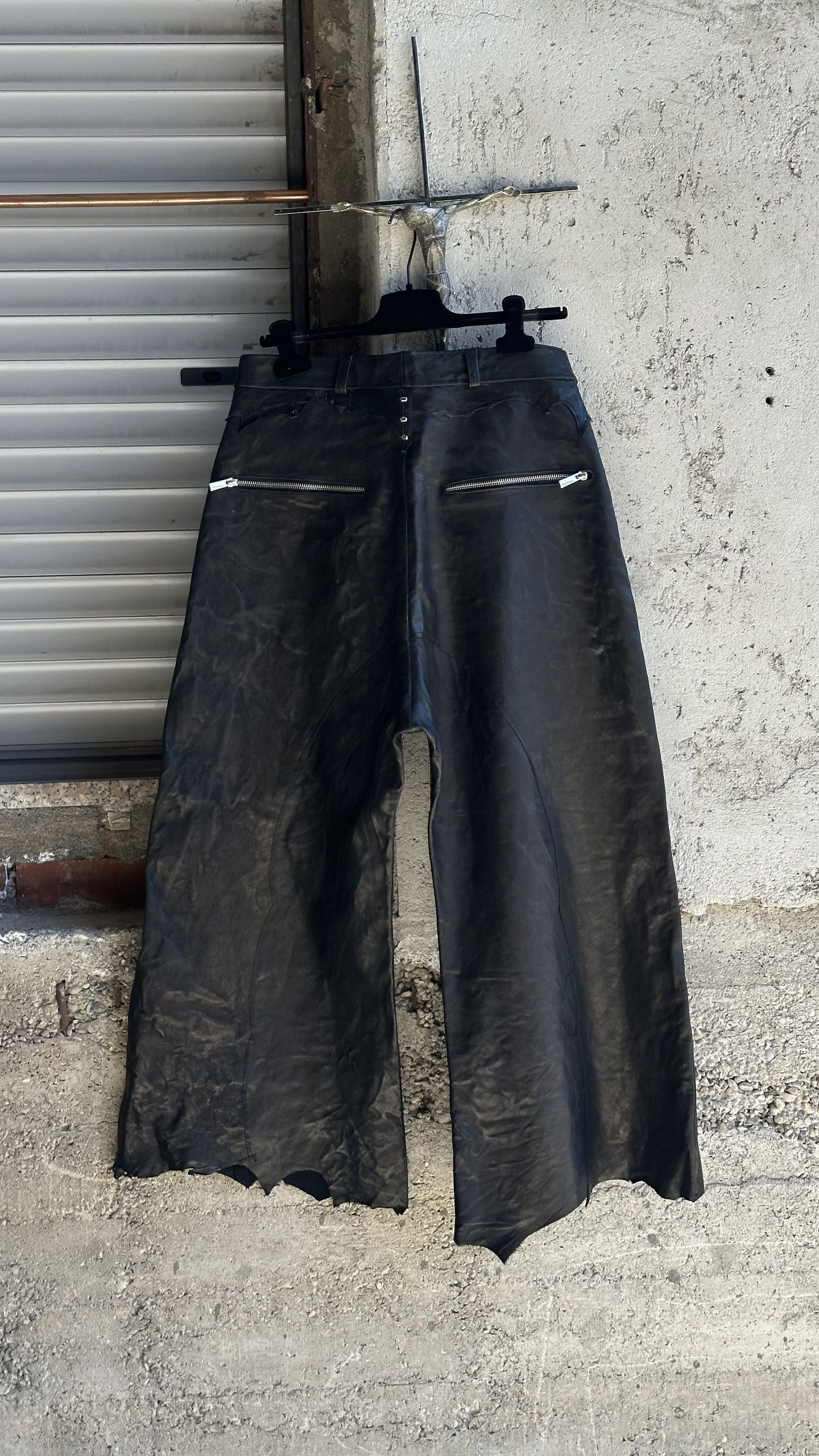 Gli stessi pantaloni in pelle nera visti da dietro, con due tasche con zip e l'orlo tagliato irregolare.