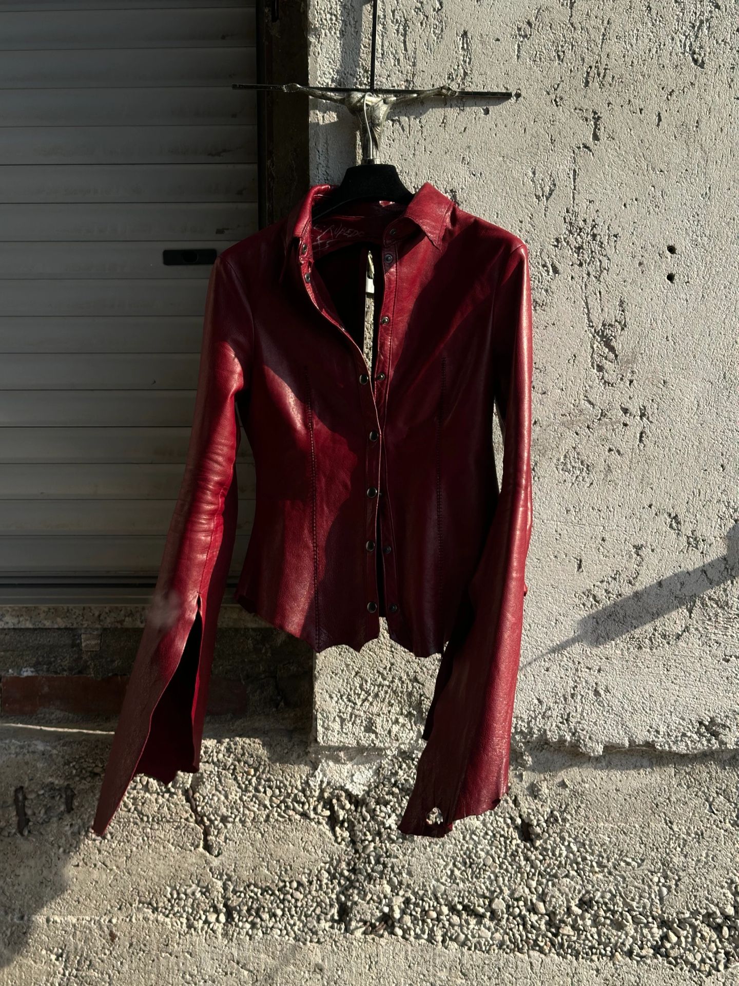 La camicia rossa appesa sotto un crocifisso, vista frontale.