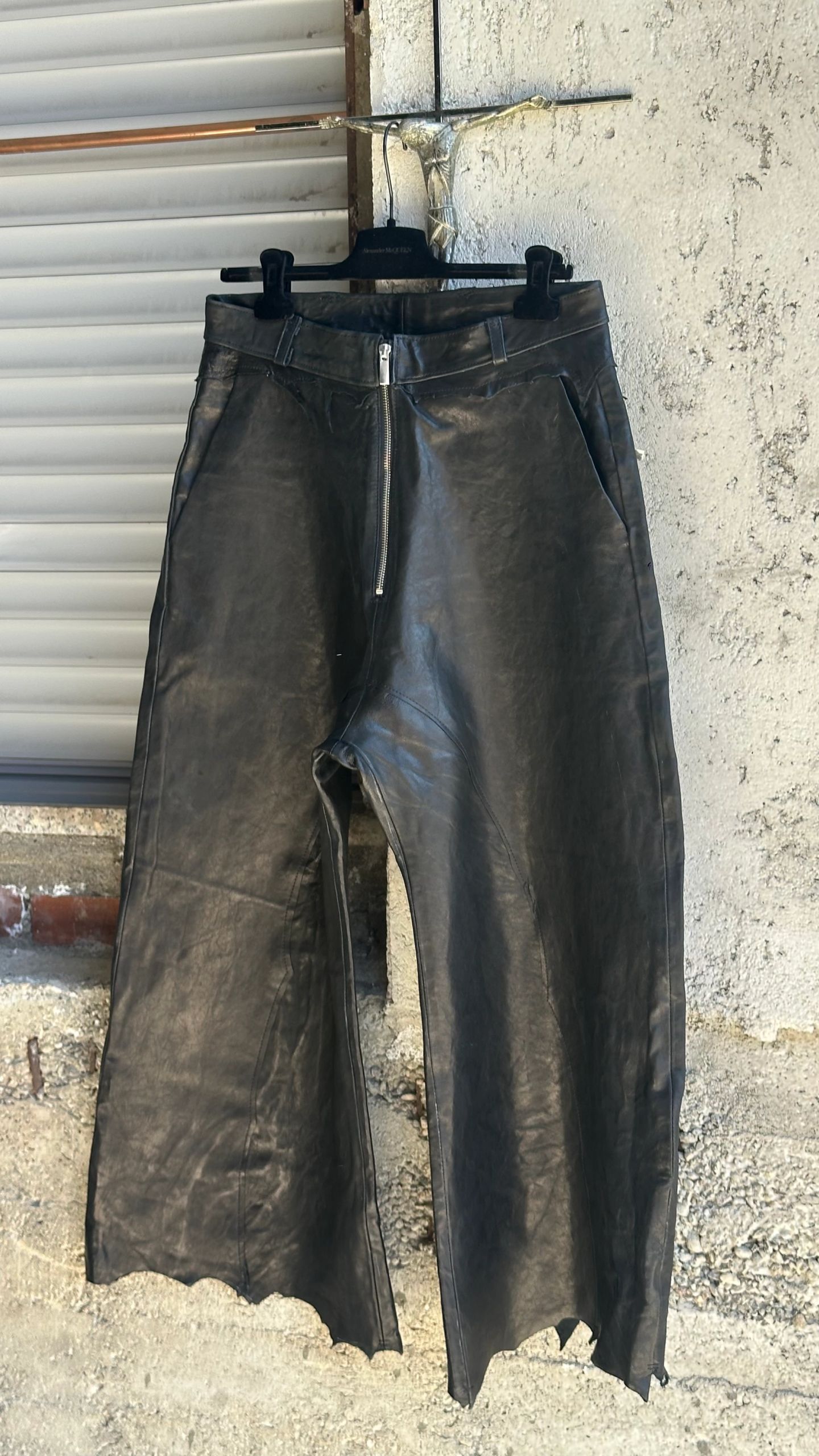 Pantaloni ampi in pelle nera, vista frontale, con zip a vista e orlo grezzo.