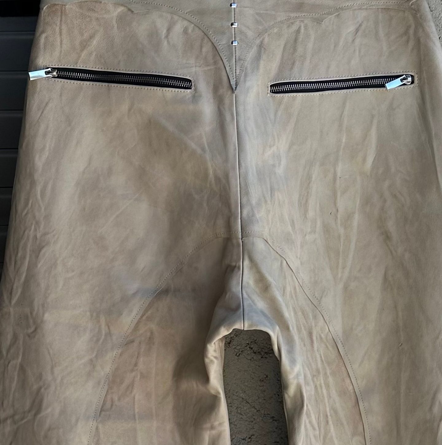 Due tasche con zip a filetto sul dietro dei pantaloni chiari.