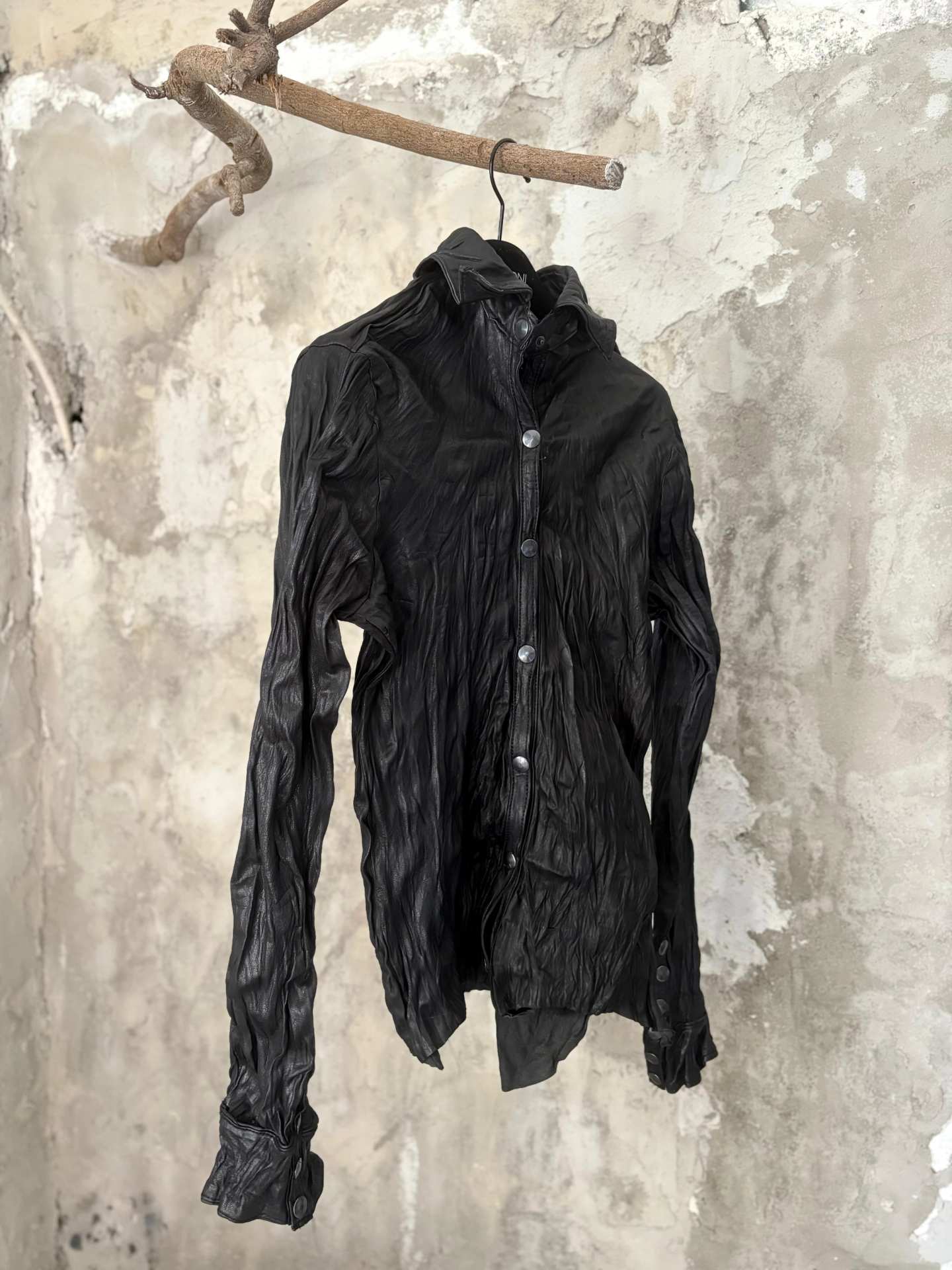 La stessa camicia in pelle nera vista piu da vicino, contro il muro di cemento.