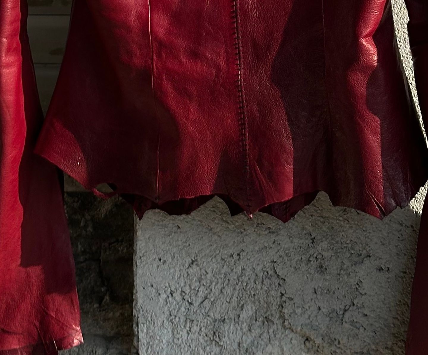 Orlo grezzo e smerlato della giacca rossa, contro il muro di cemento.