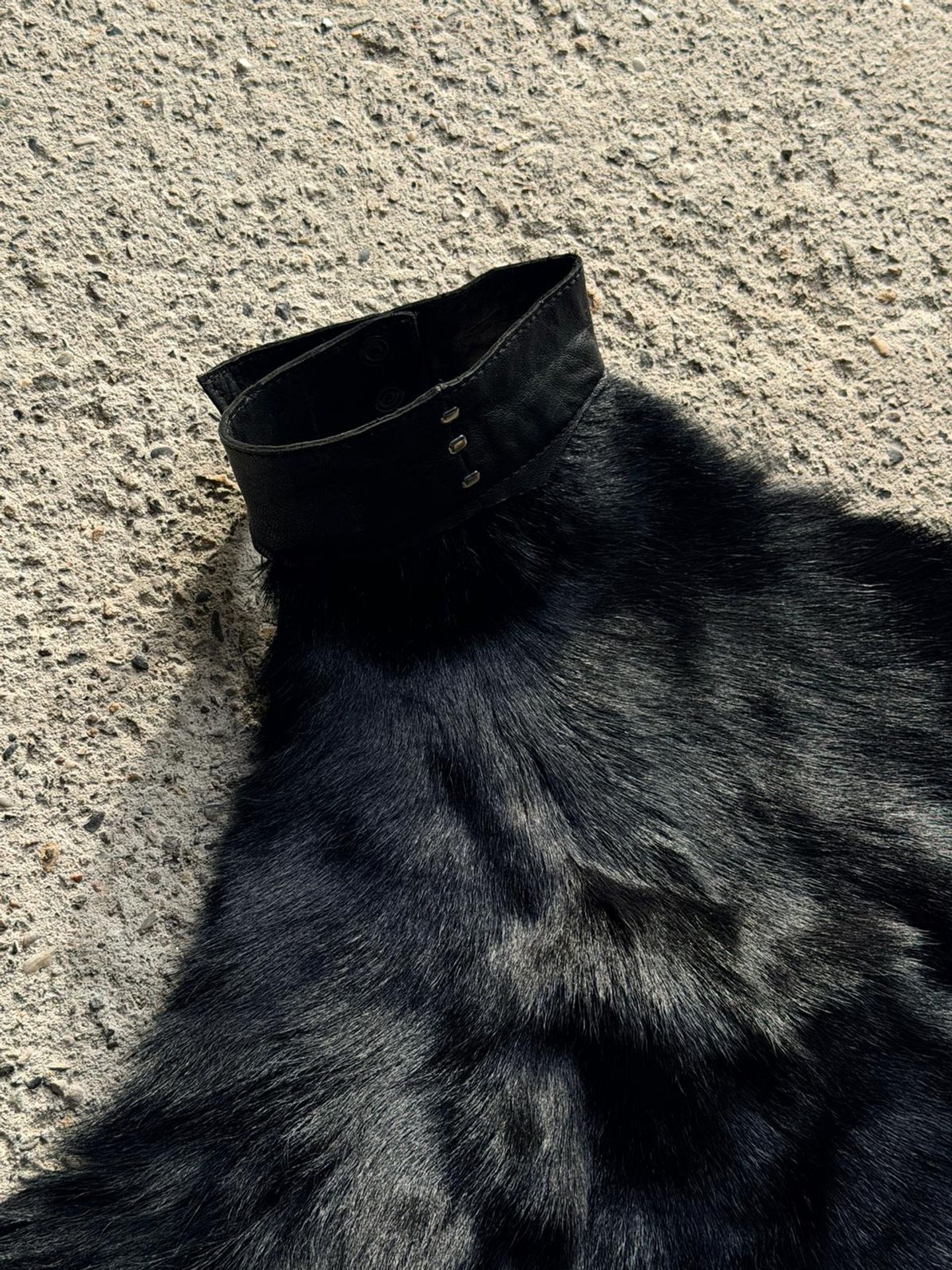 Il top in pelliccia di capra disteso sul cemento, con il collo in pelle e i fili di cucitura.