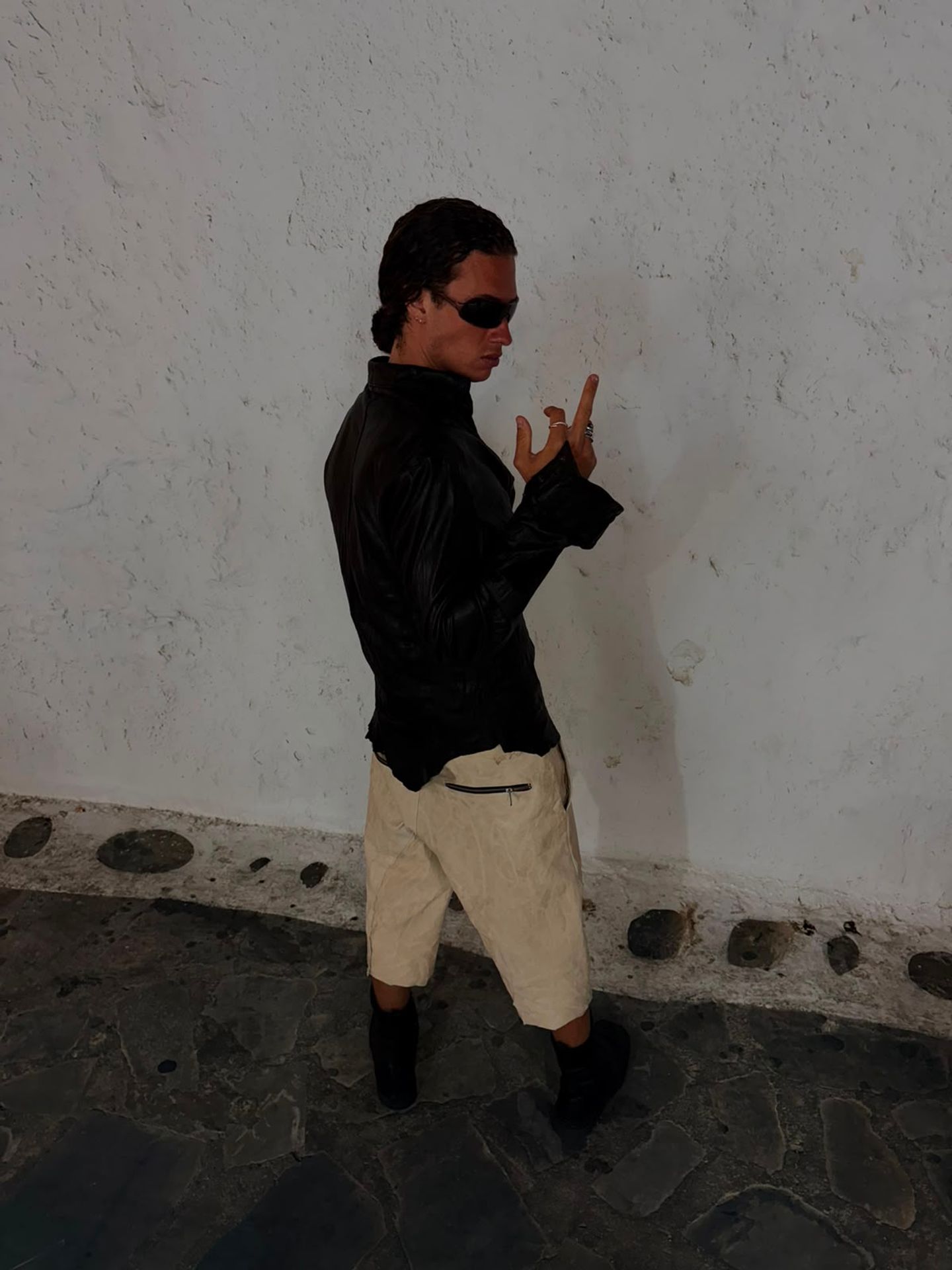 Uomo con pantaloni corti chiari in pelle, contro un muro bianco.