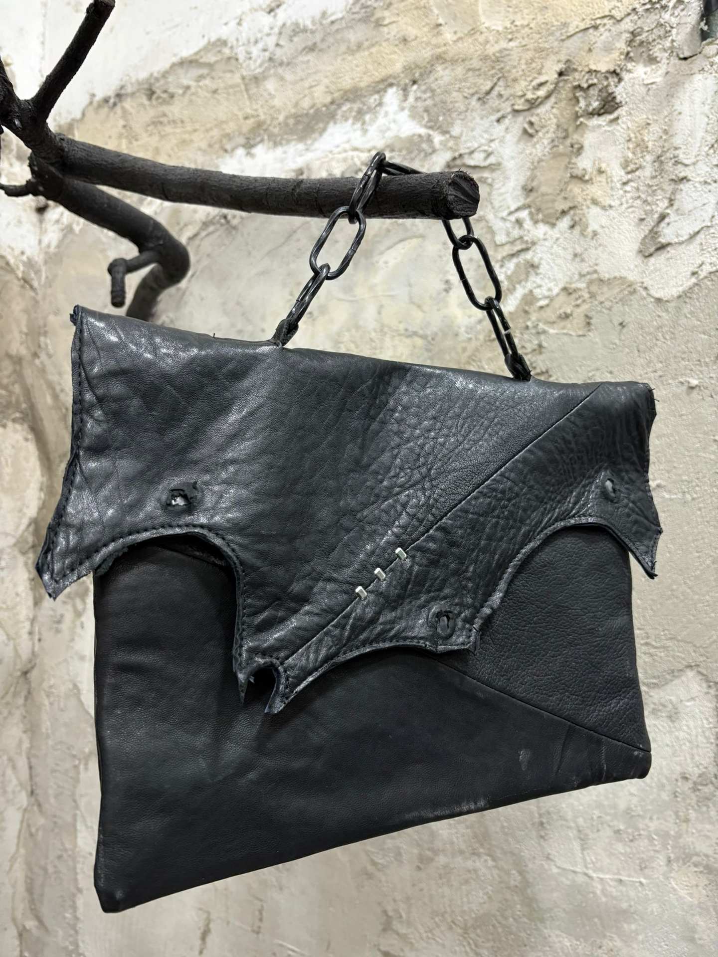 La borsa in pelle nera appesa a un ramo con una catena, con la patta sagomata.