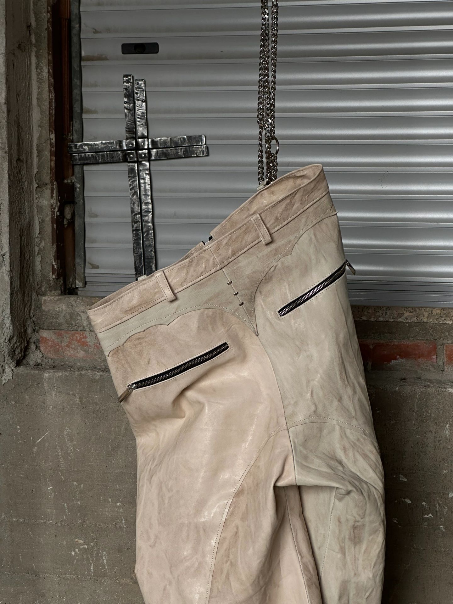 Pantaloni chiari in pelle appesi dentro una cornice di metallo nero.