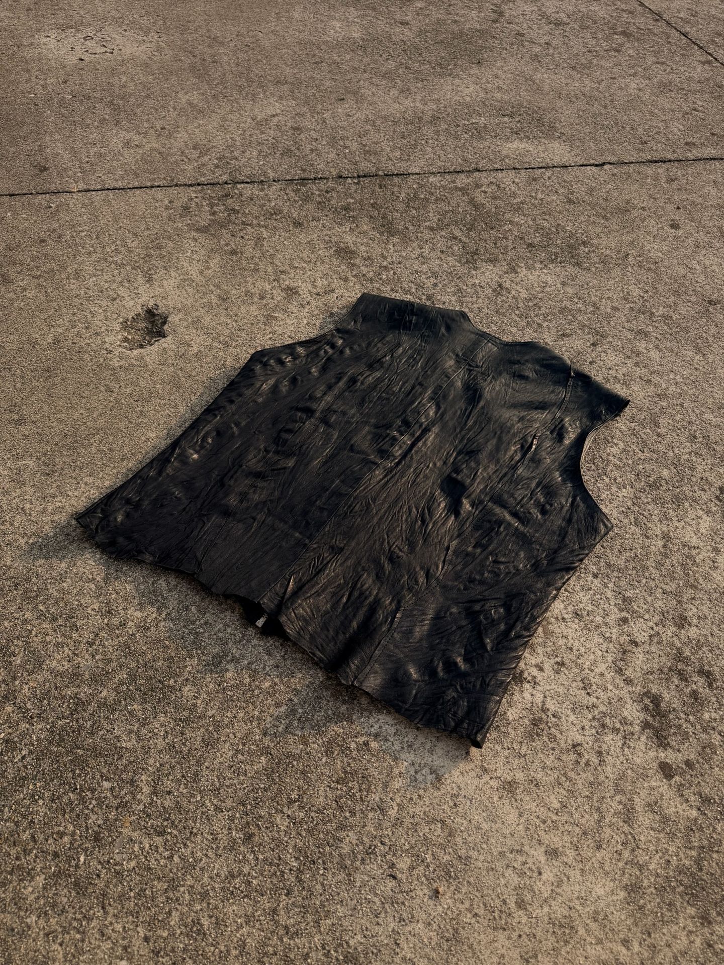 Un secondo gilet in pelle nera disteso sul cemento, visto di sbieco.