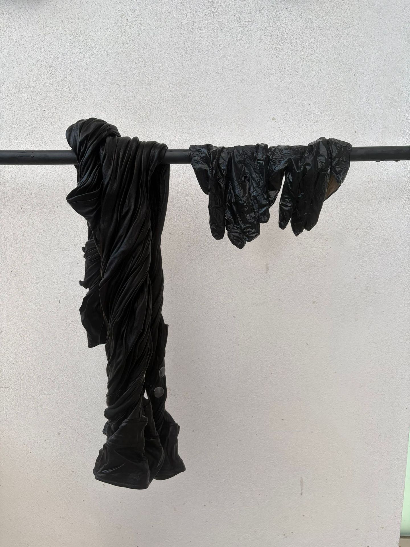 Capi neri appena tinti, appesi ad asciugare su una barra davanti a un muro chiaro.