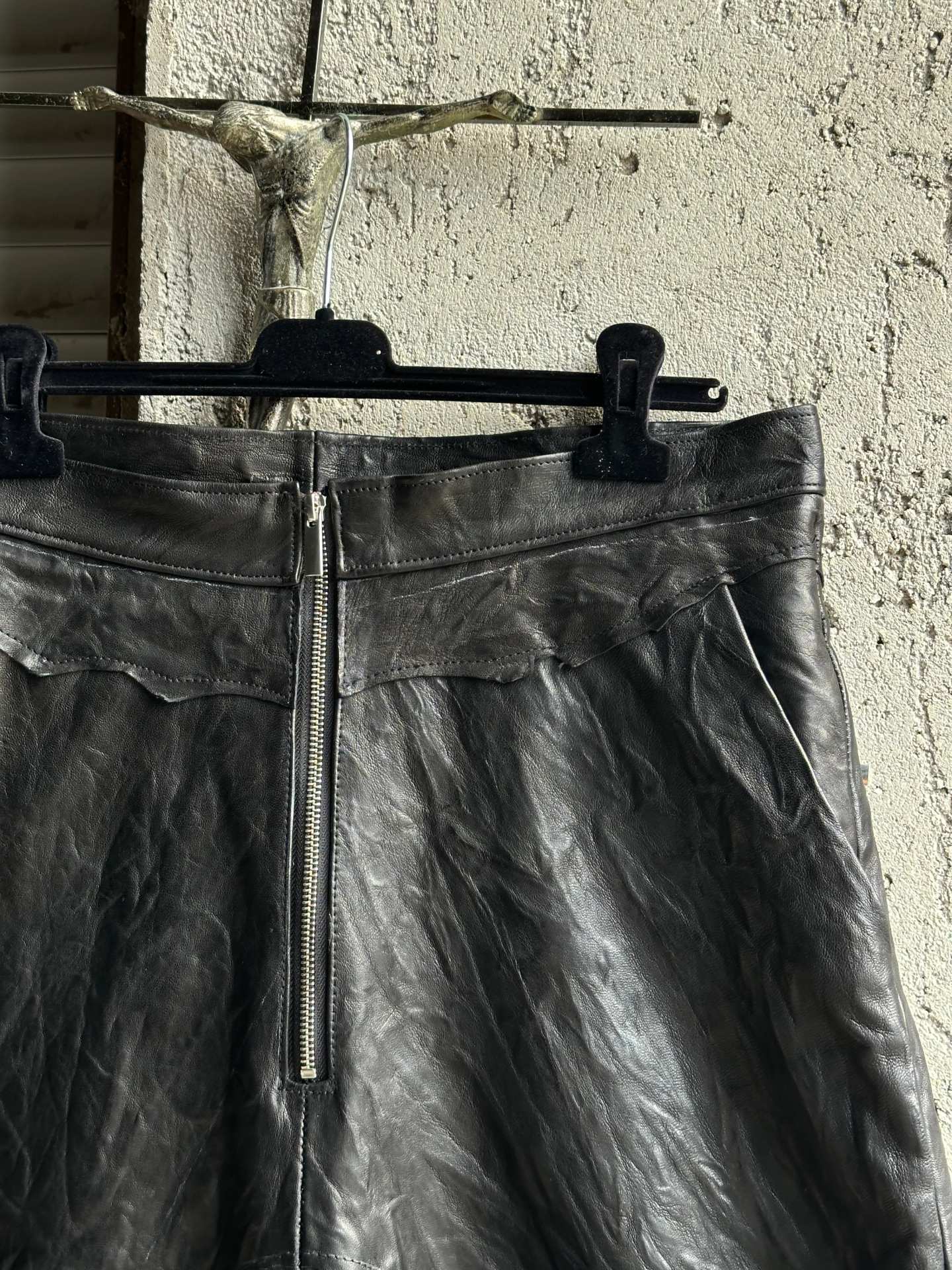 I pantaloncini in pelle appesi a una gruccia davanti a una serranda, visti da davanti.
