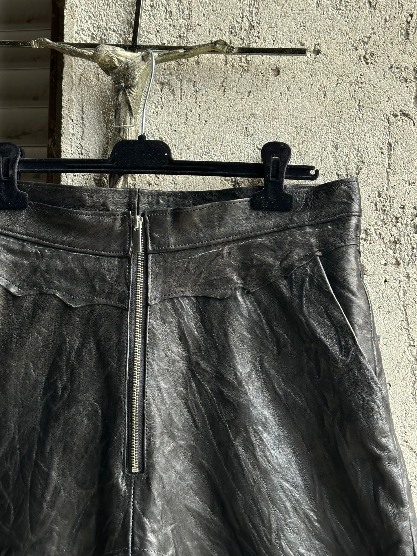 I pantaloncini in pelle appesi a una gruccia davanti a una serranda, visti da davanti.