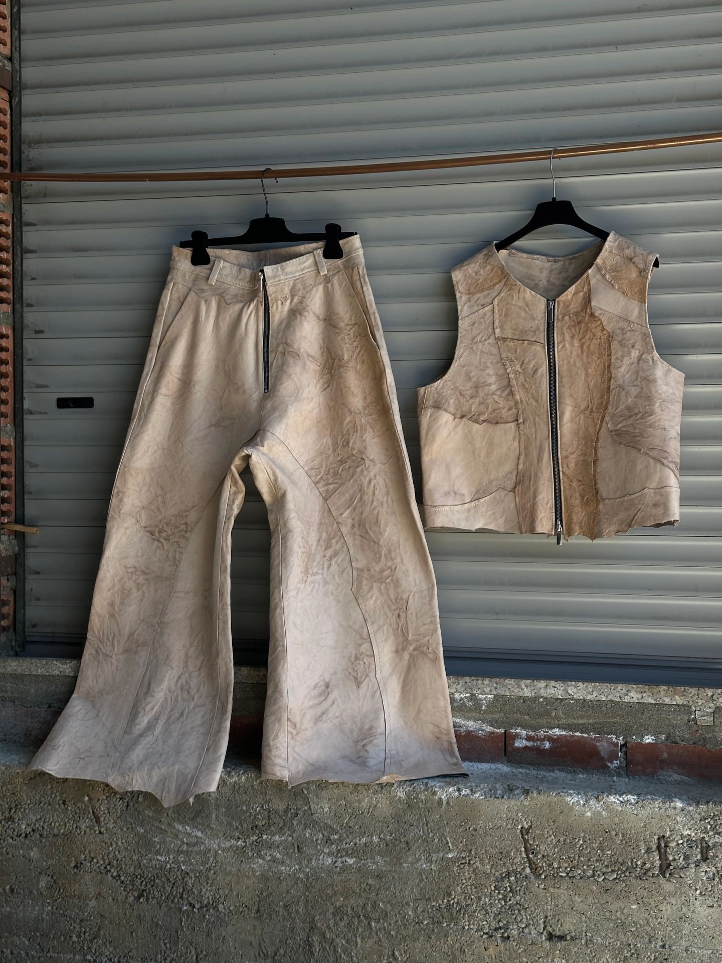 Pantaloni chiari e gilet appesi insieme davanti a una serranda.