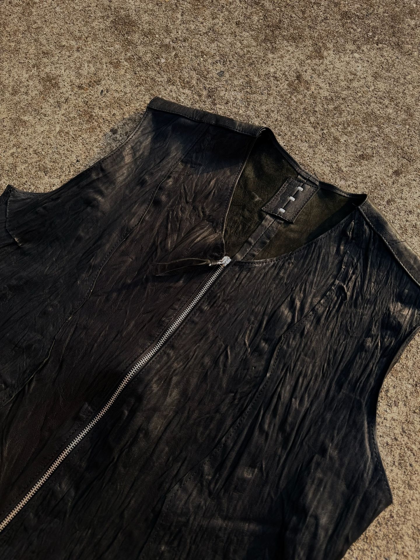 Dettaglio di un capo in pelle scura con una zip lunga, disteso.
