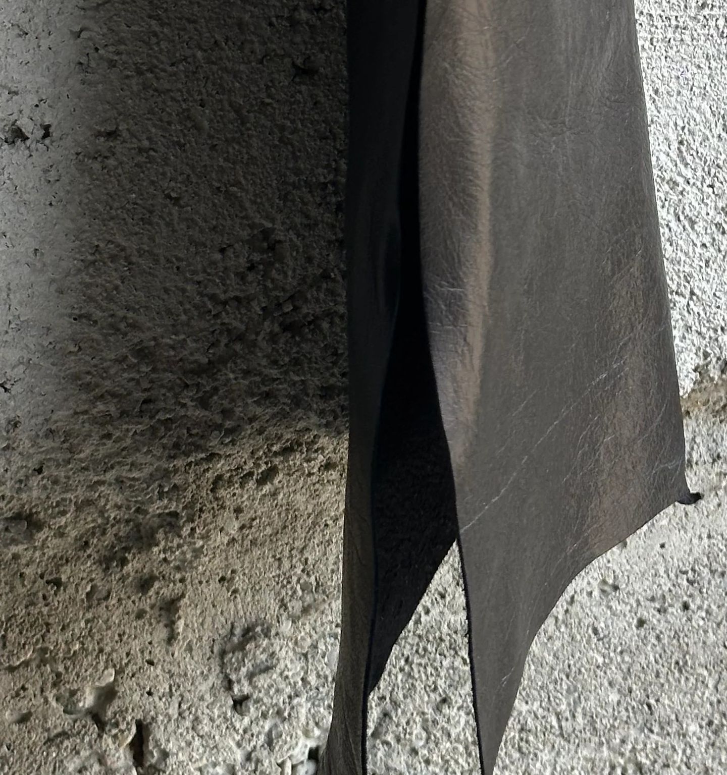 Orlo appuntito e non rifinito della camicia in pelle nera, contro il cemento chiaro.