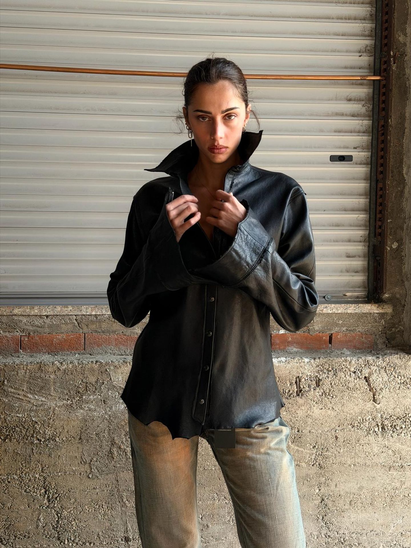 Modella con camicia in pelle nera dal collo alto, davanti a una serranda.
