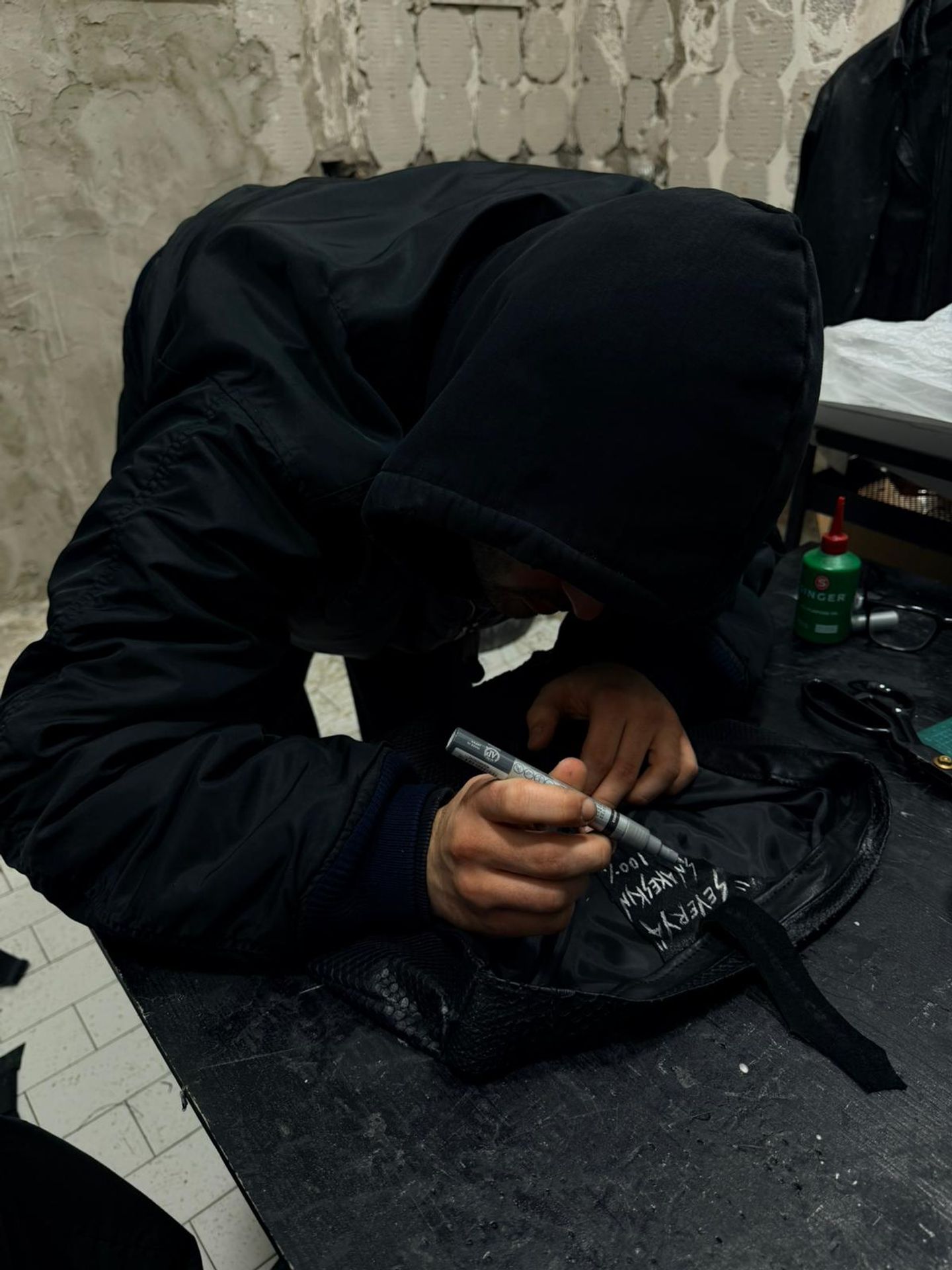 Le mani di chi fa le Creature mentre scrive a mano il nome e la composizione su un capo in pelle nera.