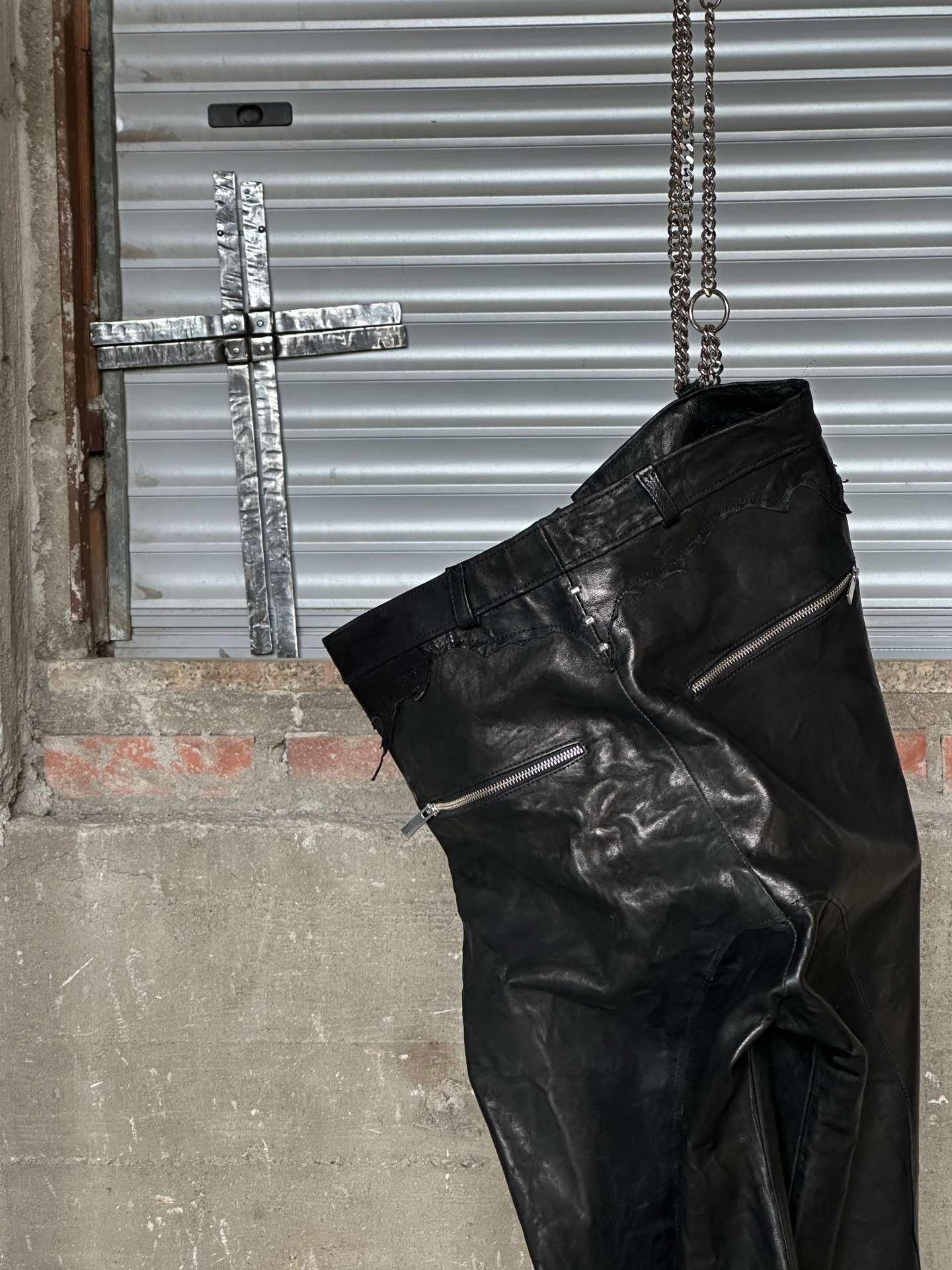 Dettaglio ravvicinato degli stessi pantaloni in pelle nera, con zip e pieghe profonde.
