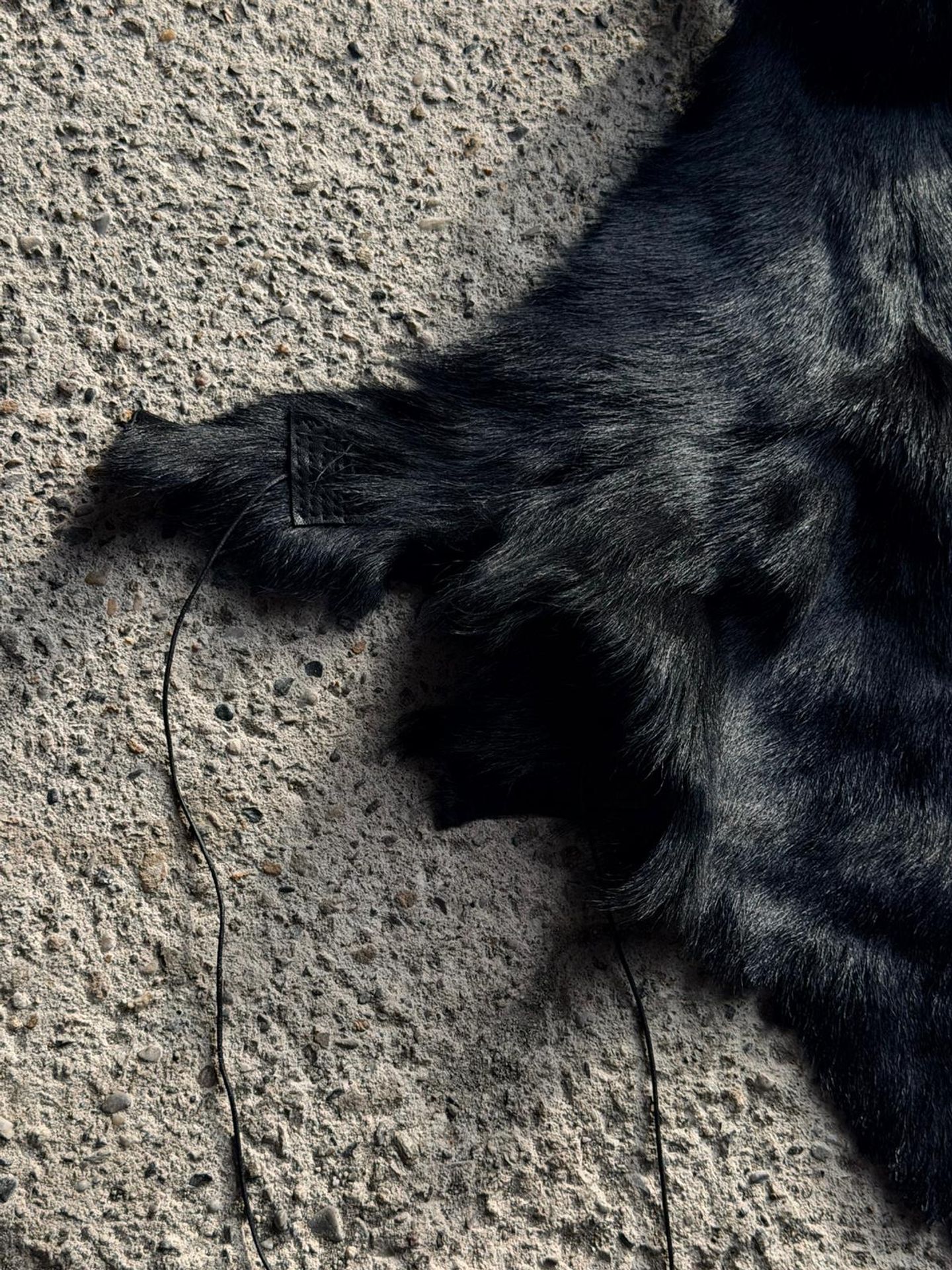 Dettaglio della pelliccia nera con la linguetta di pelle e i fili di cucitura.