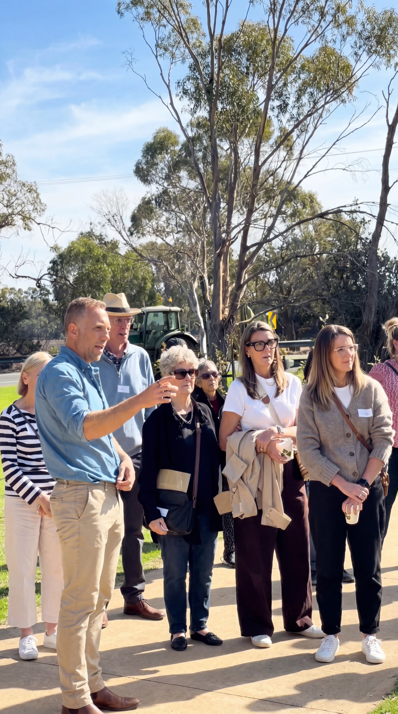 Open Day visitors gathered by a lake for a memorial tree ceremony under gum trees.