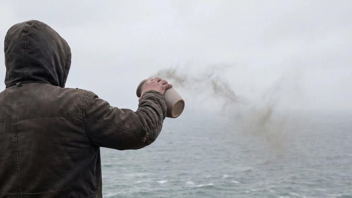 Person scattering cremation ashes over the ocean from an urn
