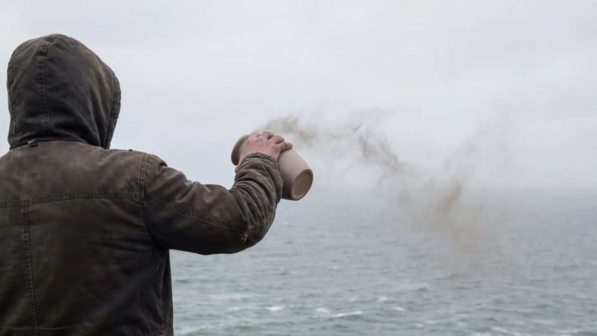 Person scattering cremation ashes over the ocean from an urn