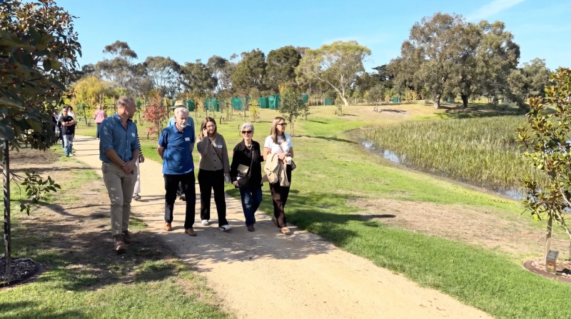 Guests touring Mornington Green Living Legacy Gardens on open day, walking past the lake and tree plantings.