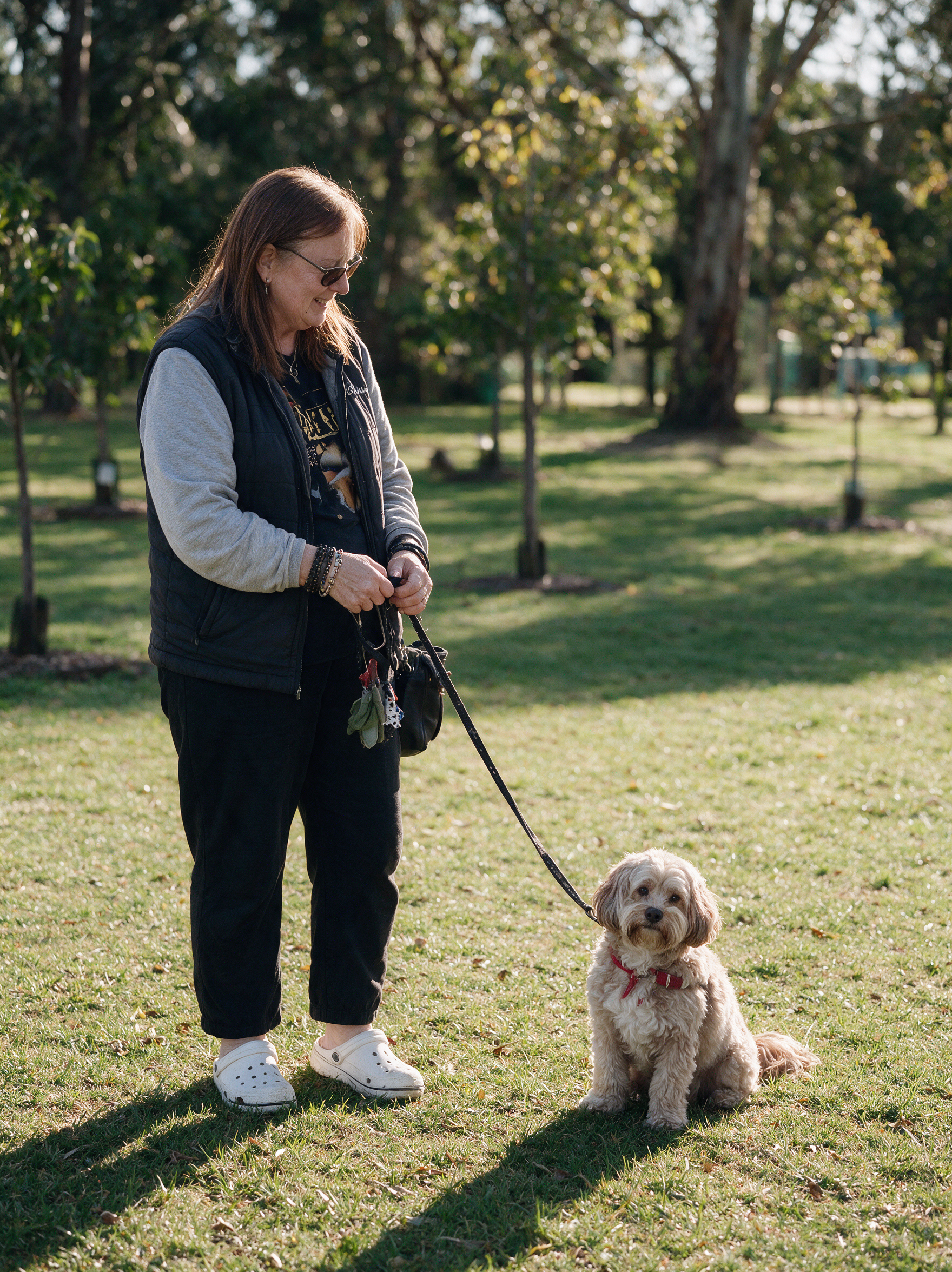 Woman holding a leash and standing outdoors with her small tan dog sitting on the grass