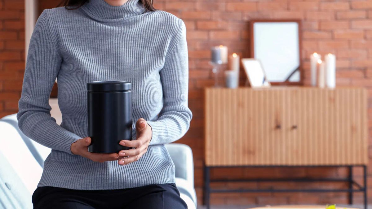 Woman holding a black cremation urn in a home setting
