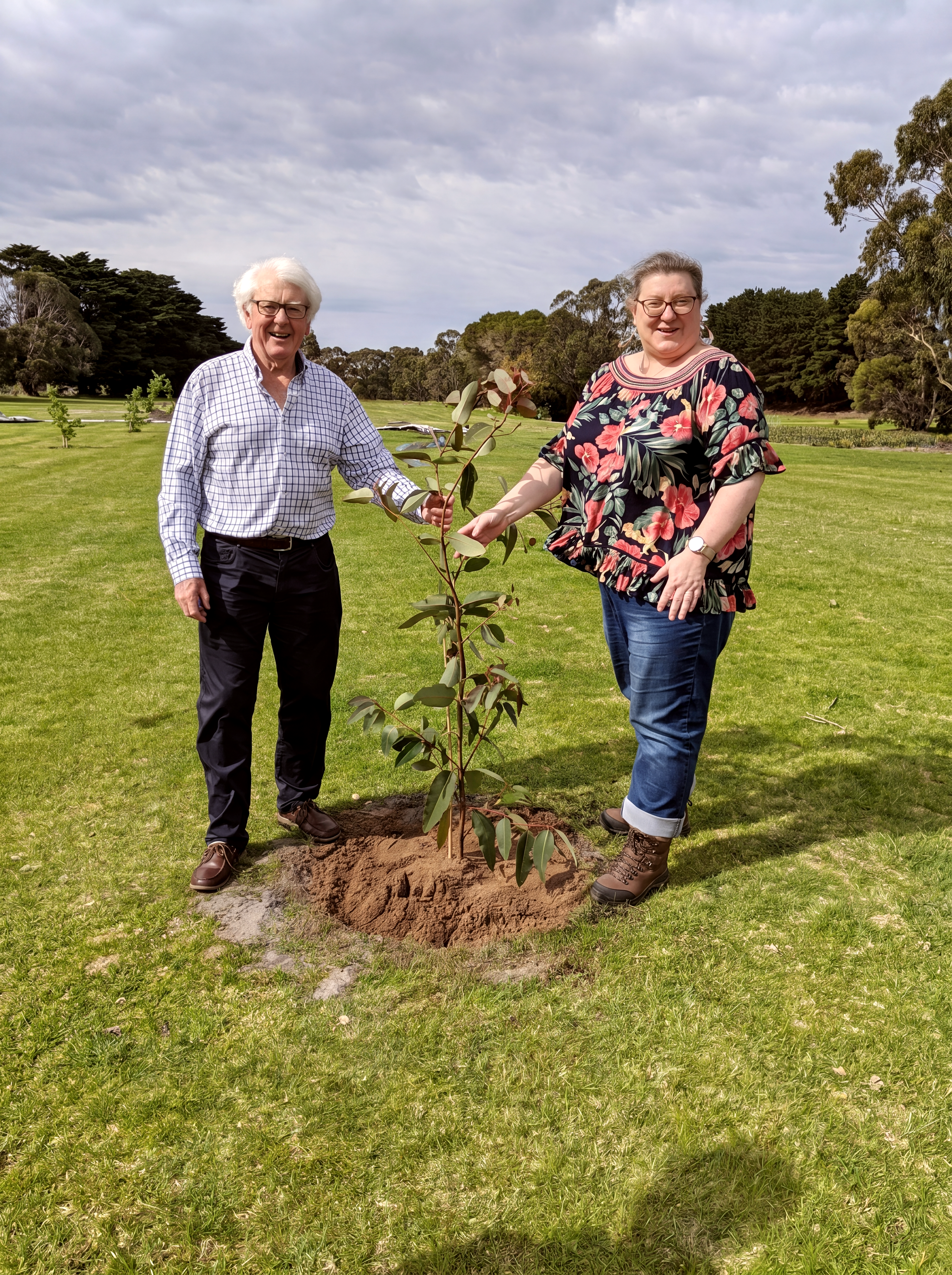 Two people with a newly planted tree in a memorial garden.