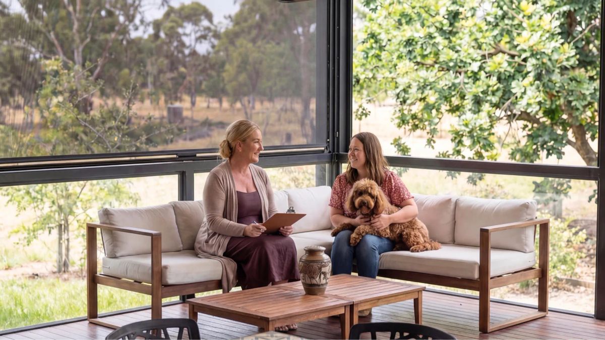 Woman receiving pet loss counselling while holding her dog, sitting on a sofa with a memorial urn in a peaceful setting.