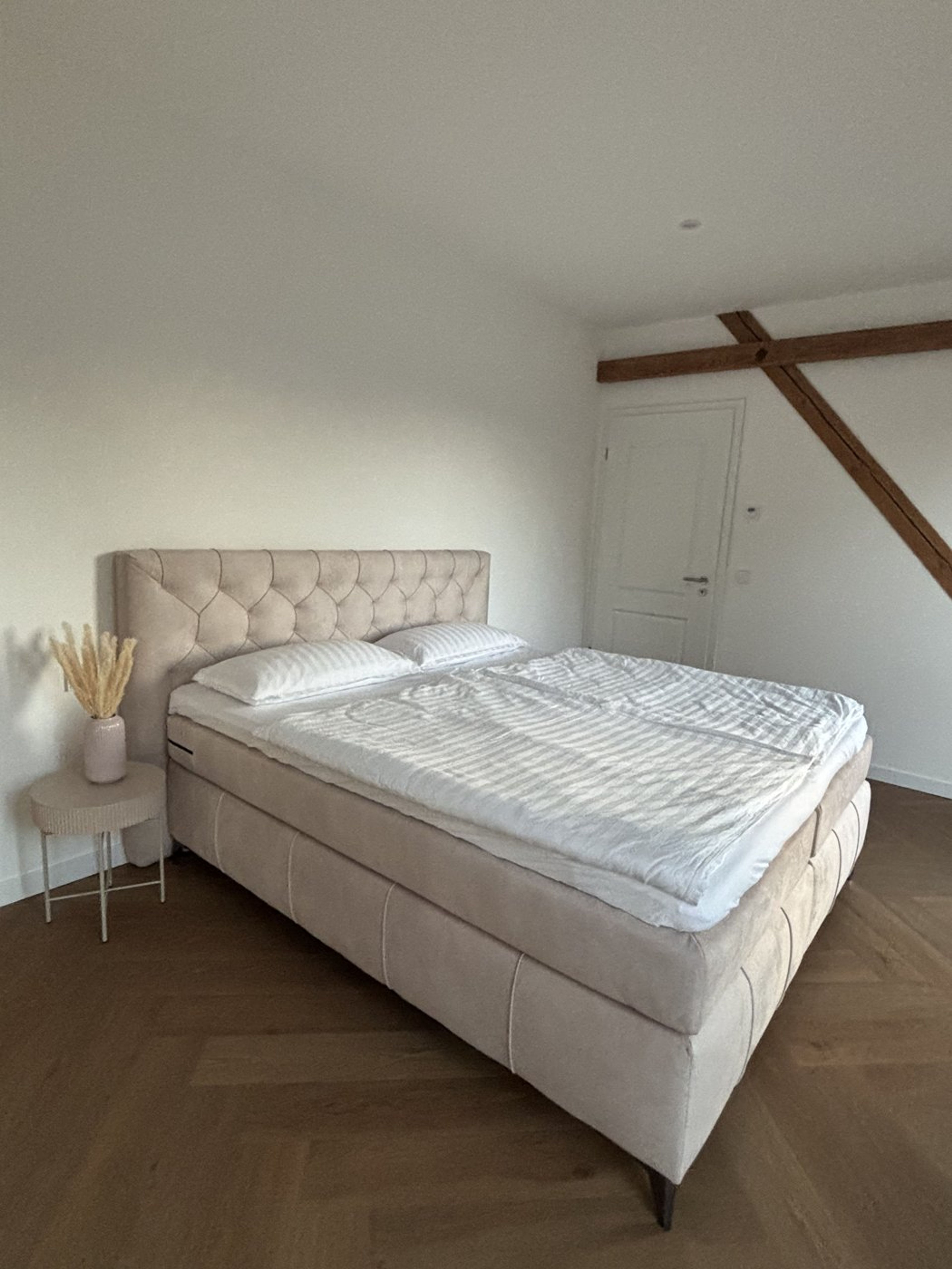 Schlafzimmer mit gepolstertem Boxspringbett und Pampasgras