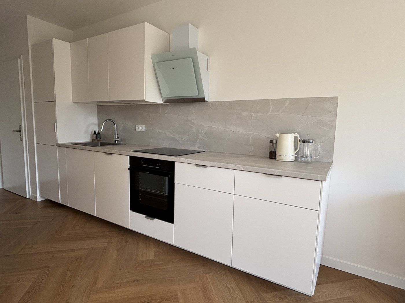 Weiße Einbauküche mit Marmor-Rückwand und Induktionskochfeld