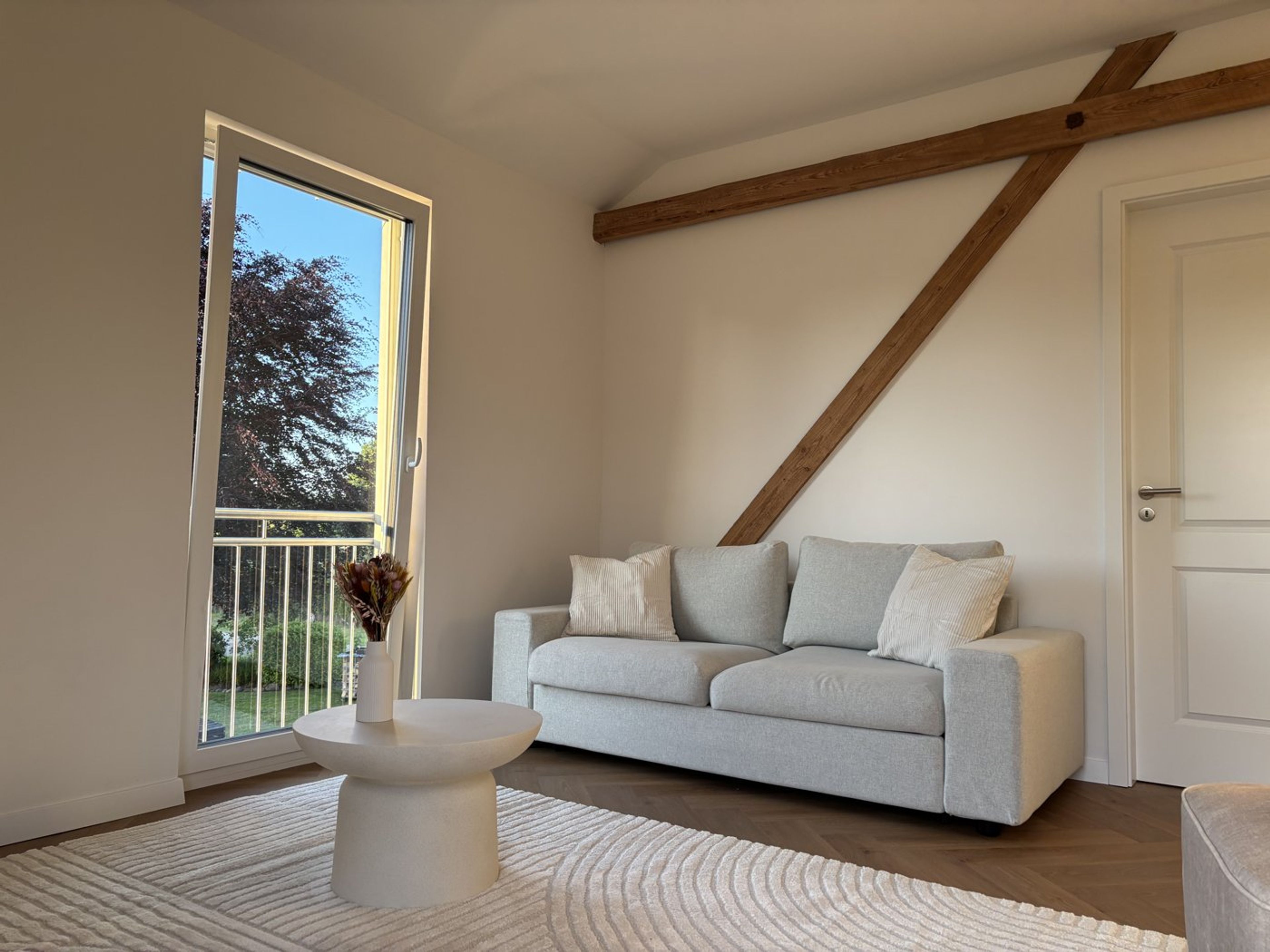 Helles Wohnzimmer mit grauem Sofa, Holzbalken und Trockenblumen