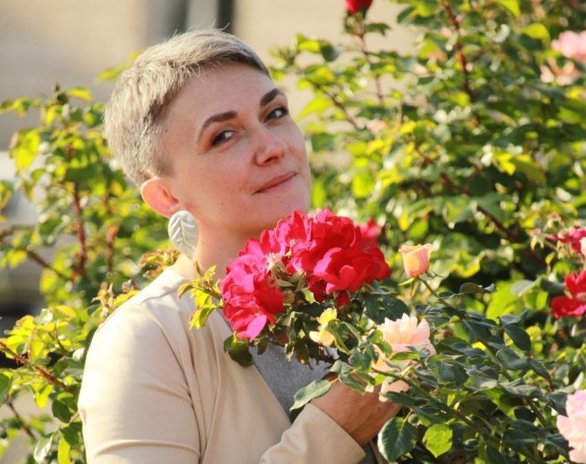 A woman stands near blooming roses