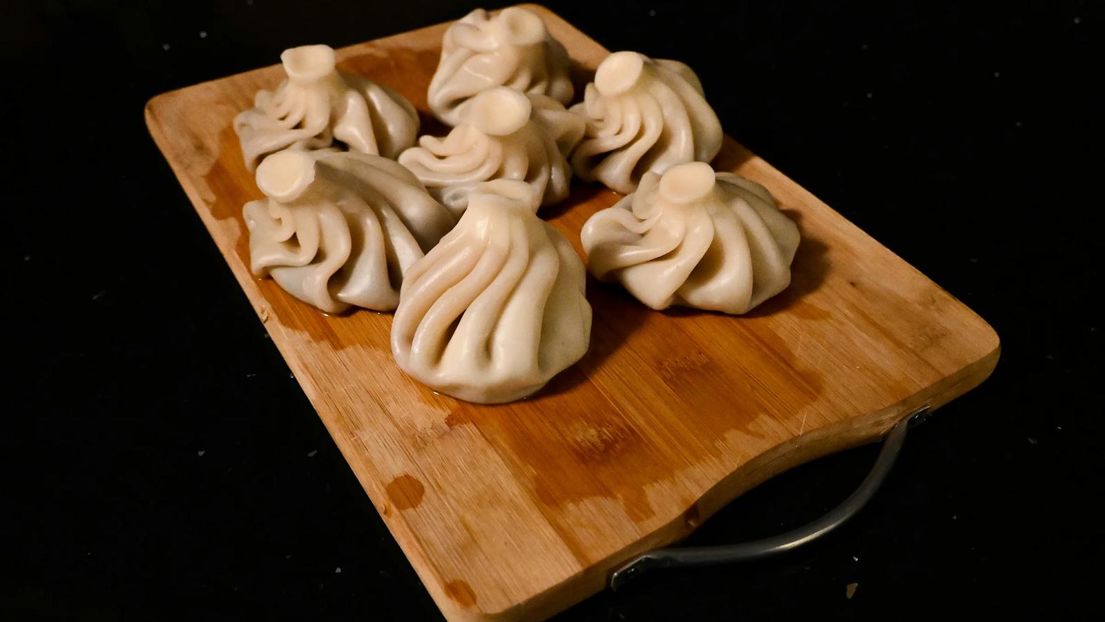 a wooden cutting board topped with dumplings on top of a table