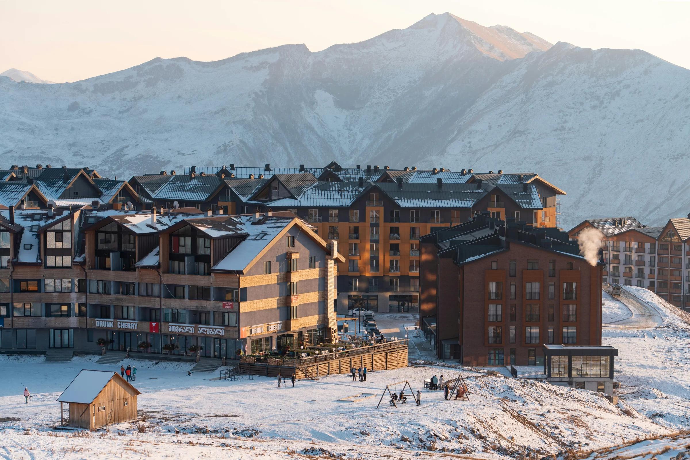 a group of buildings in the snow with mountains in the background