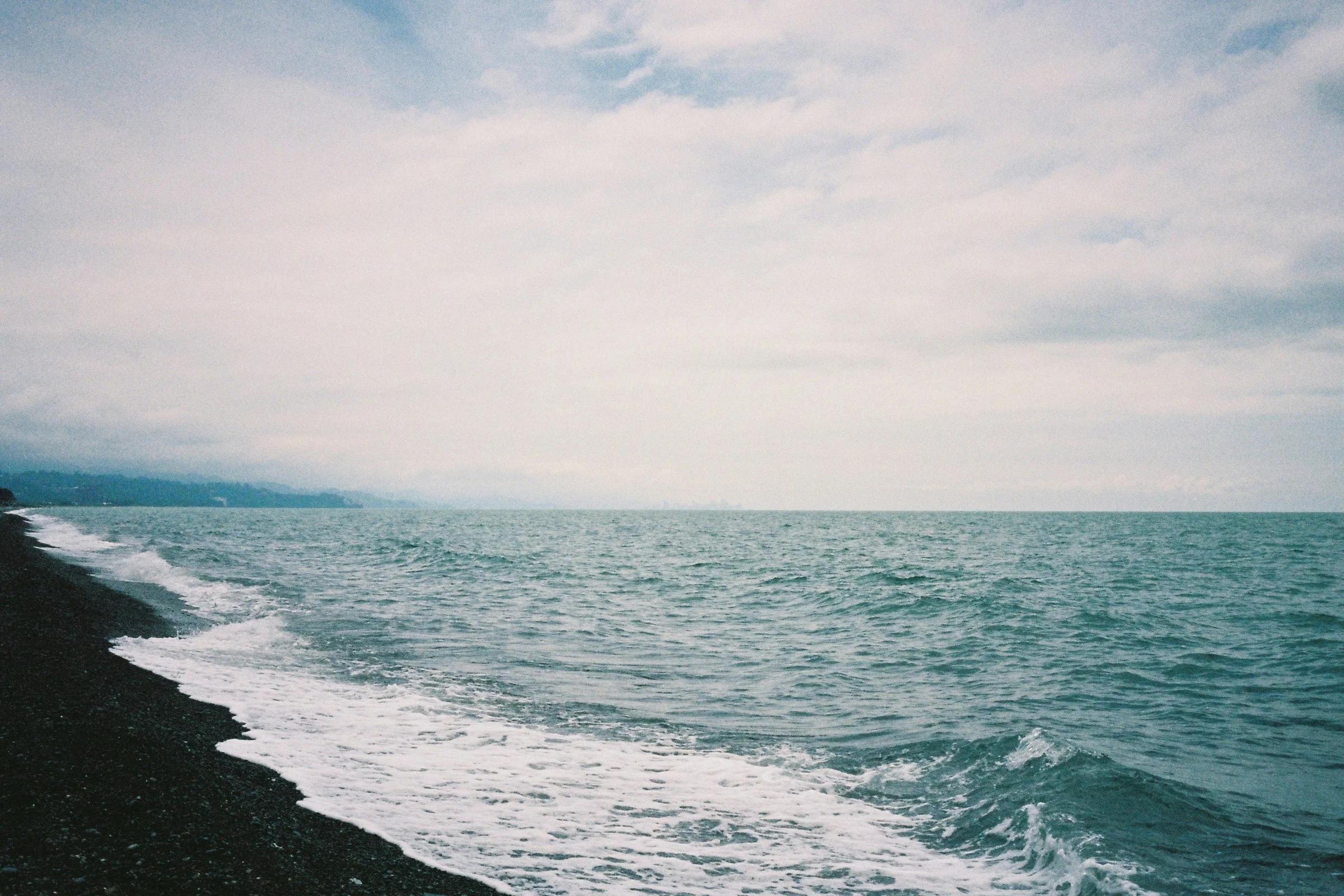 Waves crash onto a rocky shoreline under a cloudy sky.