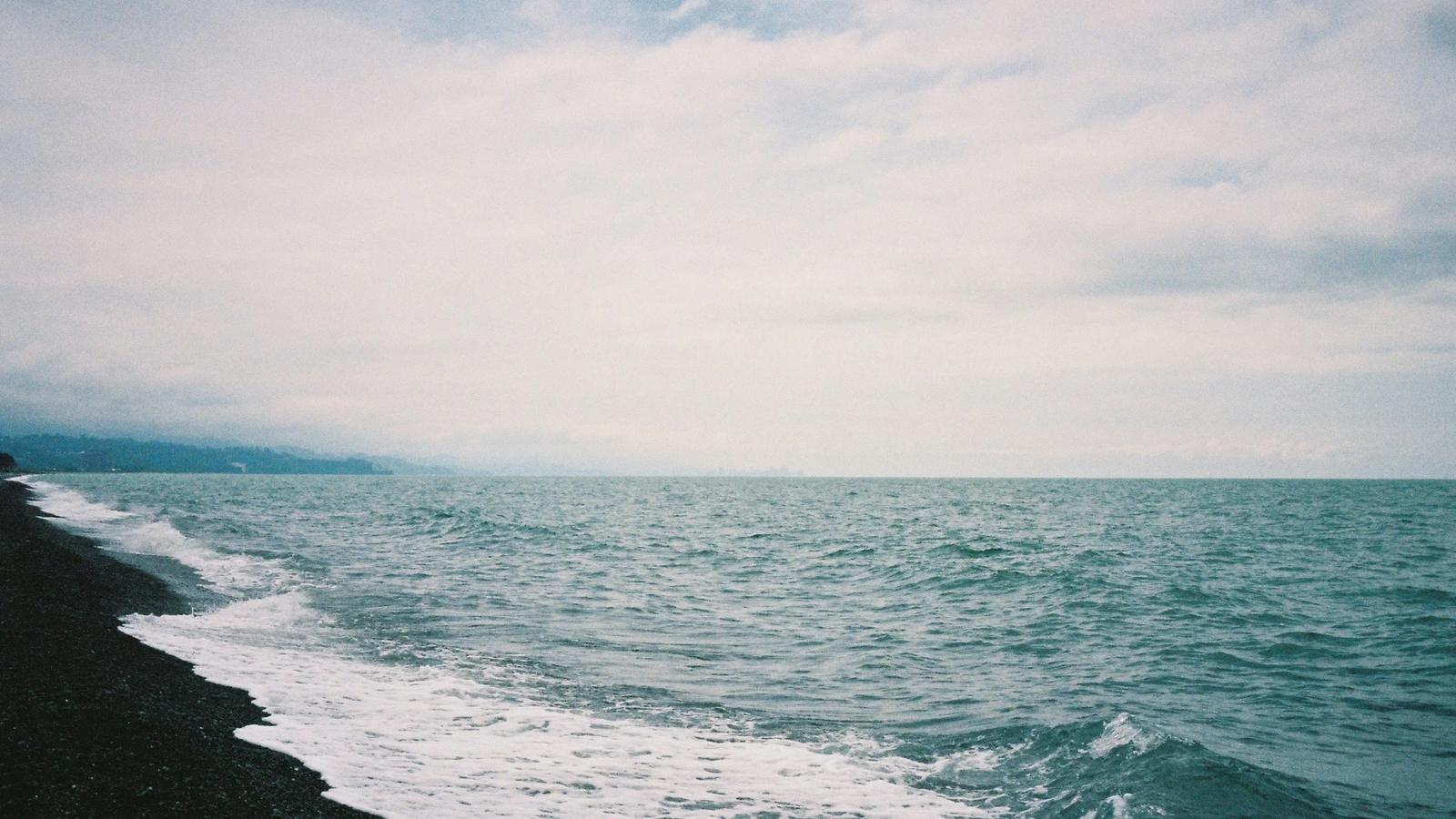 Waves crash onto a rocky shoreline under a cloudy sky.