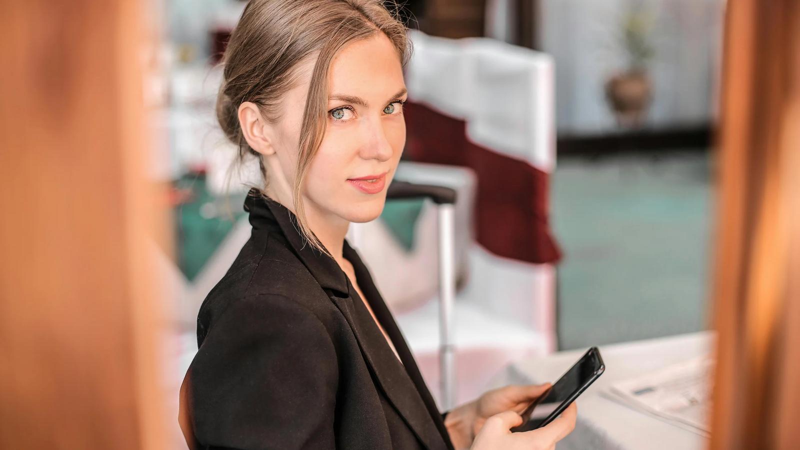 Женщина в черном пальто держит черный смартфон