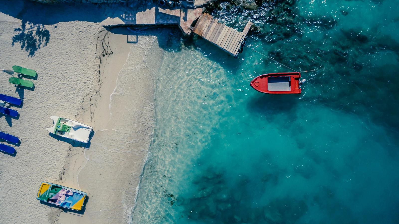 red boat on body of water near brown wooden foot board