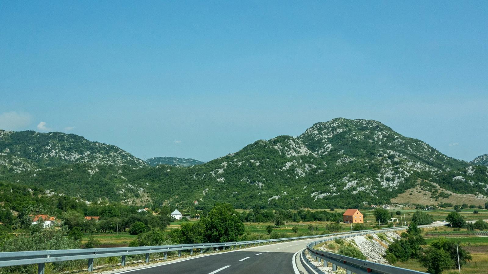gray concrete road near green mountain under blue sky during daytime