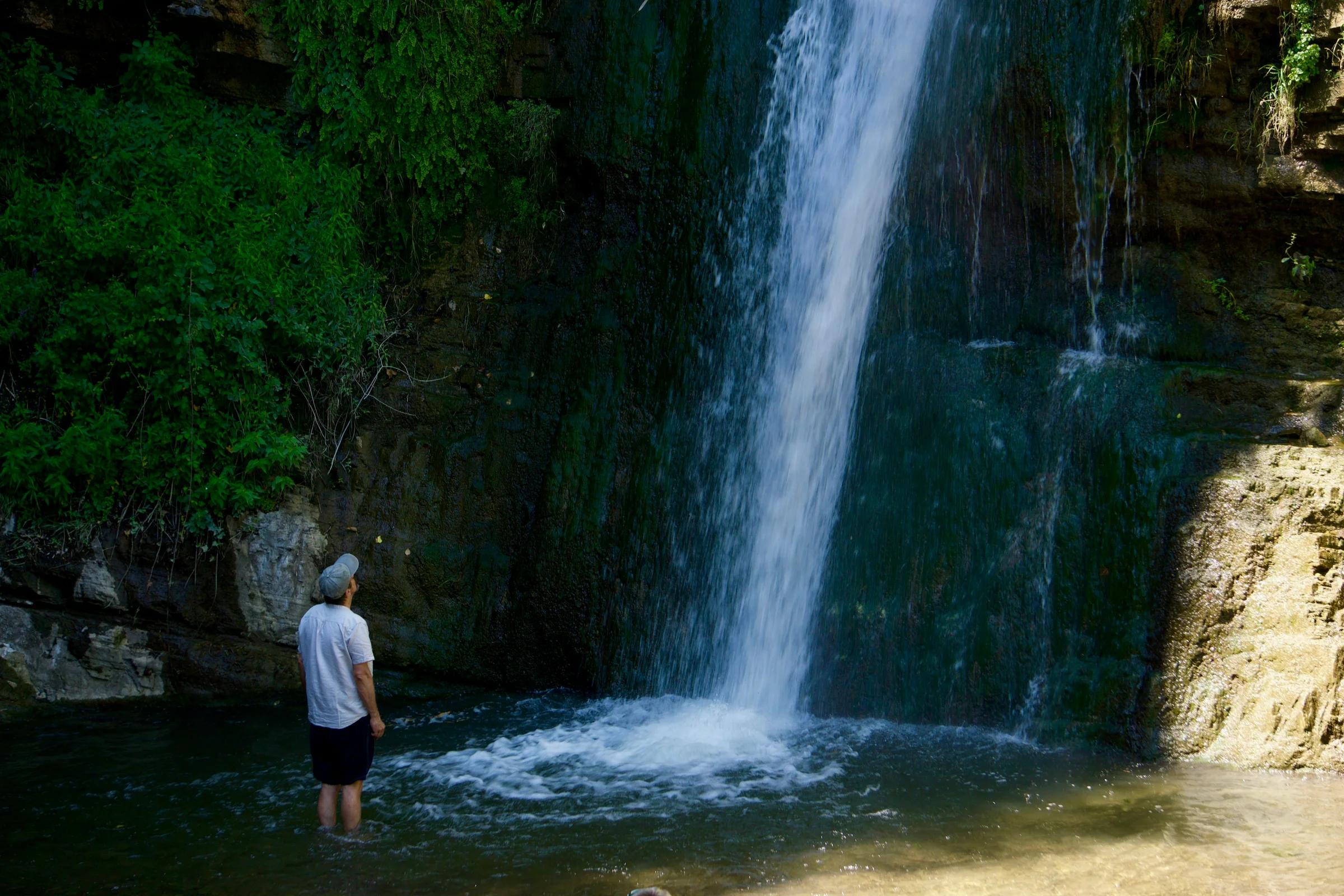 a man standing in the water near a waterfall
