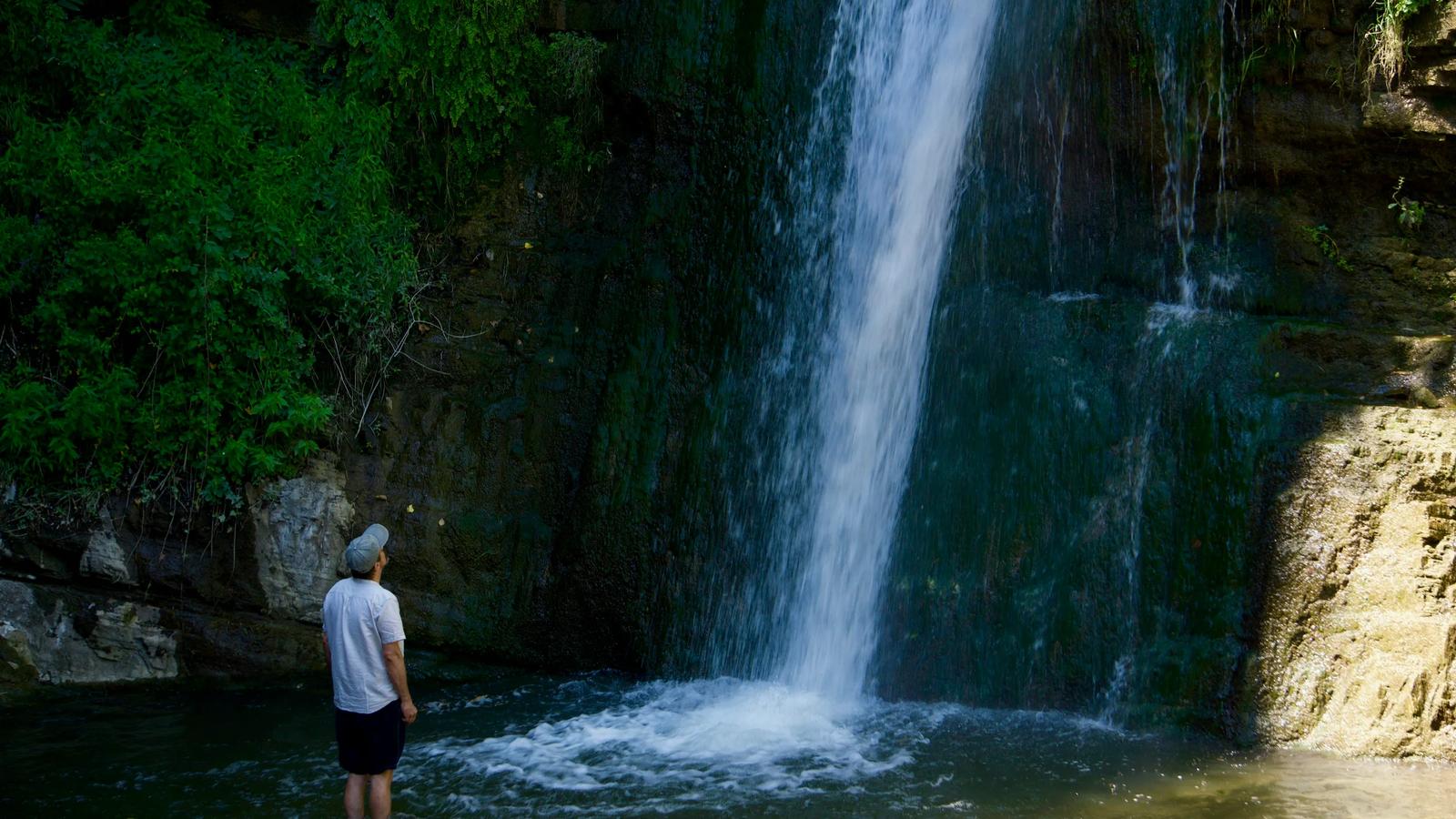 a man standing in the water near a waterfall
