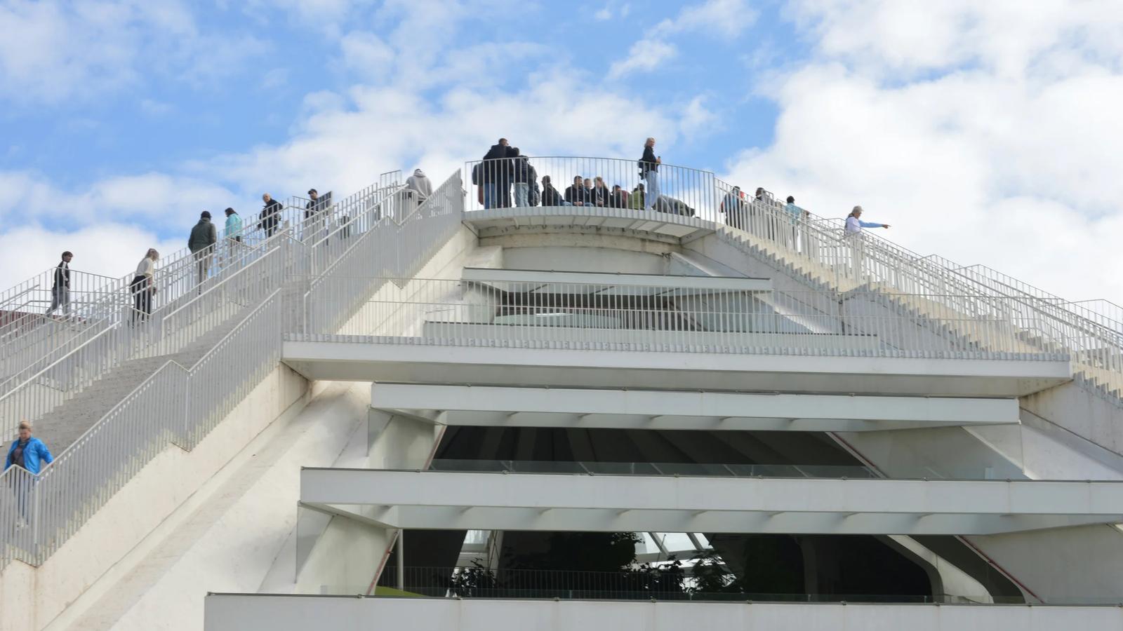 People ascend a modern pyramid-shaped building