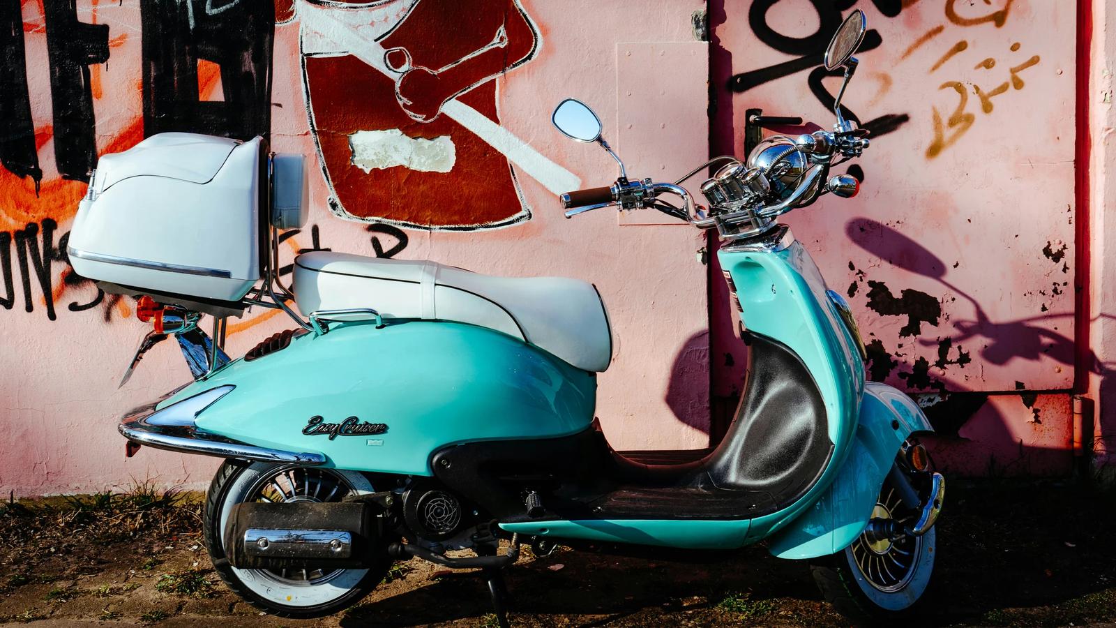 blue and black motor scooter parked beside wall with graffiti