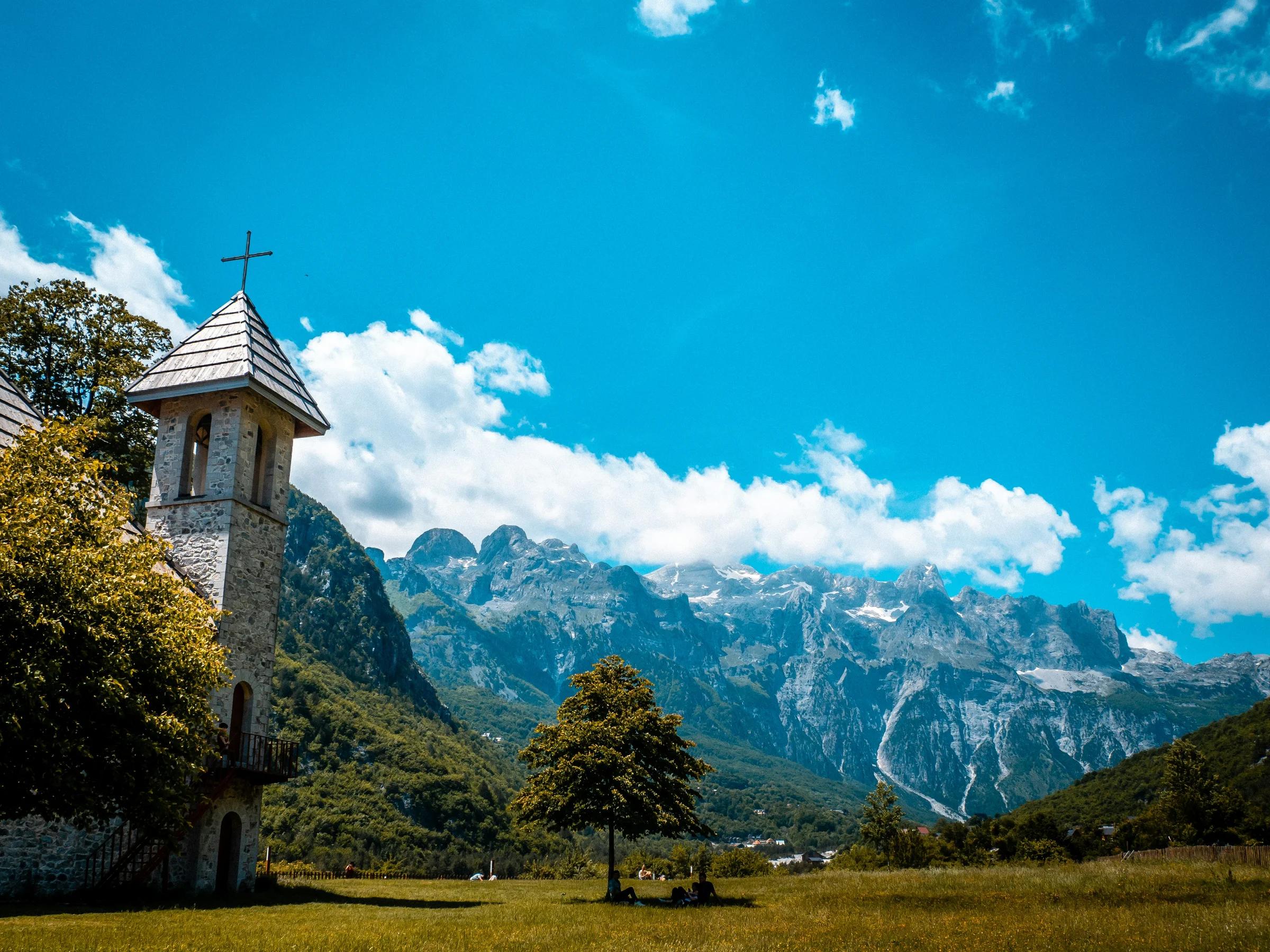A church stands before majestic mountains and blue skies.