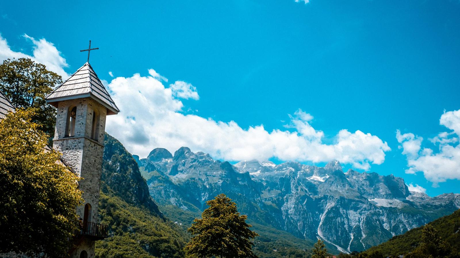 A church stands before majestic mountains and blue skies.